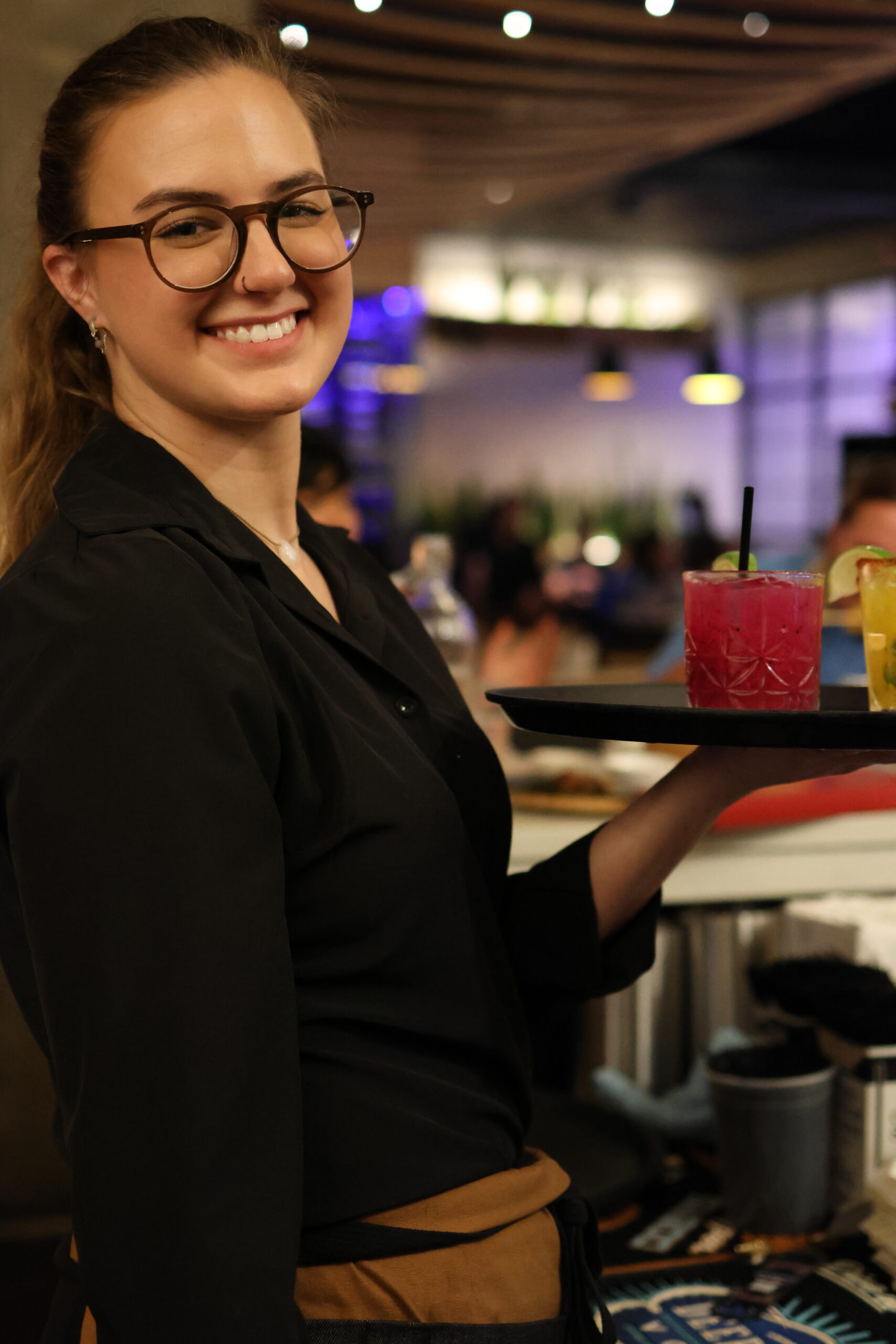 Waitress serving cocktail in busy restaurant.