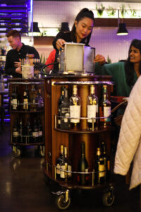 Server preparing drinks at cocktail cart in restaurant.