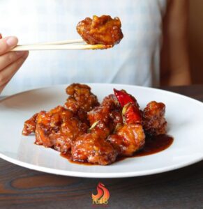 Person eating spicy saucy chicken with chopsticks.