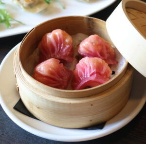 Pink dumplings in a bamboo steamer basket.