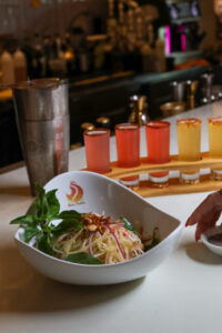 Vegetable dish with colorful drinks on bar counter.